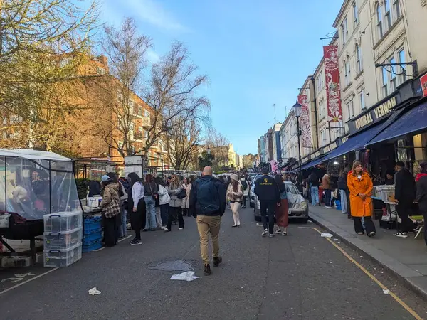 Londra, İngiltere - 3.29.2025: Notting Hill 'deki Lively Portobello Road Market kalabalığı tezgahlara göz atıyor ve açık mavi gökyüzü altında cadde boyunca yürüyor