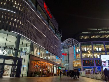 Londra, İngiltere - 11.9.2024: Geceleri Westfield alışveriş merkezinin modern cephesinde Primark ve West Elm gibi önde gelen perakende mağazalarının önünden geçen insanlar