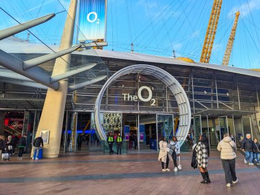 Londra, İngiltere - 12.30.2024: Güneşli bir günde belirgin sarı direklerin altında Greenwich Yarımadası 'ndaki büyük bir eğlence merkezi olan The O2 Arena' nın ana girişine yakın ziyaretçiler
