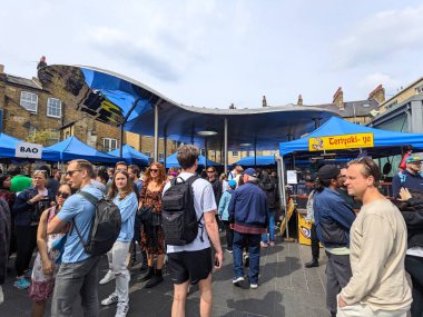 Londra, İngiltere - 30 Nisan 2023: Değişik bir kalabalık Greenwich gıda pazarında toplanıyor, Teriyaki ve Bao gibi tezgahları mavi tuğlalar altında geziyor