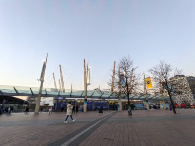 Londra, İngiltere - 13 Şubat 2023: İnsanlar O2 Arena 'nın önünden geçiyor, Londra' da akşam saatlerinde belirgin sarı direkleri ve modern cam tepe örtüsü olan sembolik bir eğlence merkezi.