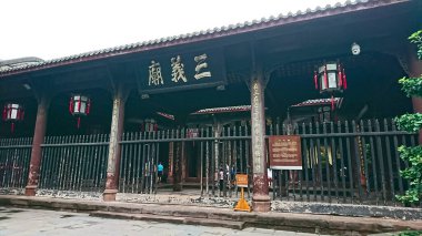Chengdu, Çin - 30 Haziran 2018: Tarihi Sanyi Tapınağı 'nın girişi üzerine kazınmış ahşap kolonlar, asılı fenerler ve öne çıkan koyu metal bir çitle geleneksel Çin mimarisini sergiliyor.