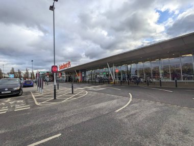 Londra, İngiltere - 17 Şubat 2023: Bir Sainsburys süpermarketinin dış görünüşü, park halindeki arabaları ve bisikletleriyle bulutlu bir gökyüzü altında banliyö alışveriş merkezinde