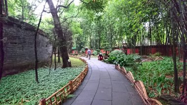 Chengdu, Çin - 6.30.2018: Bir ziyaretçi, Han Hanedanlığı 'nın Hui Anıtmezarı' nın dışındaki dolambaçlı taş patikada, yemyeşil bambu ağaçları ve çeşitli yapraklar arasında gezinir.