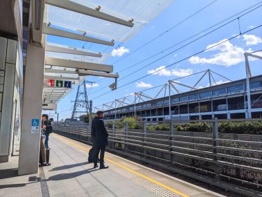 Londra, İngiltere - 4.12.2023: Yolcular ExCel Centre yakınlarındaki güneşli Elizabeth Line Custom House platformunda demiryolu ve tepe çizgileri ile modern bir tepe örtüsü altında bekliyorlar