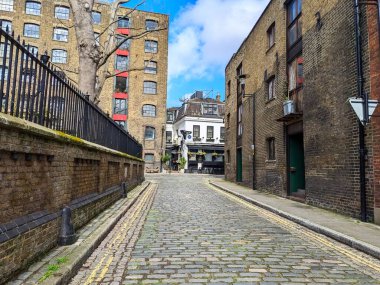 Londra, İngiltere - 22 Mart 2023: Geleneksel tuğla binalar ve tarihi Rotherhithe 'de dönüştürülmüş bir depo arasında sessiz bir kaldırım taşı caddesi esiyor.