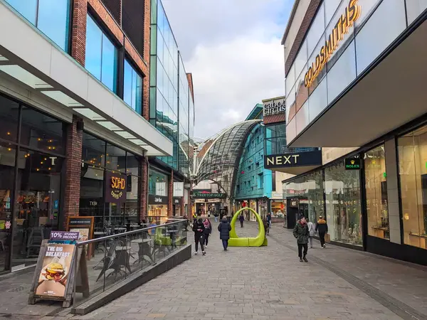 Bristol, İngiltere - 31 Ocak 2025: Cabot Circus alışveriş merkezinin kaldırımlı geçidi boyunca yürüyen yayalar, bulutlu bir gökyüzü altında cam cepheleri olan modern perakende binalar tarafından kuşatıldı