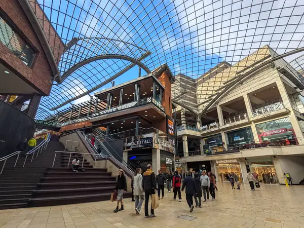 Bristol, İngiltere - 31 Ocak 2025: Müşteriler çağdaş Cabot Circus alışveriş merkezinde parlak mavi gökyüzüne sahip belirgin eğimli bir cam çatıya sahip çok katlı perakende satış alanları keşfediyorlar