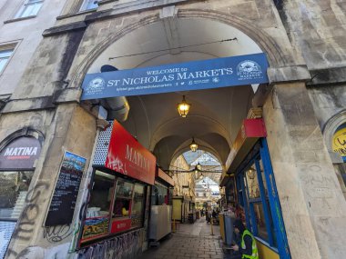 Bristol, İngiltere - 31 Ocak 2025: Tarihi St. Nicholas Pazarı 'nın kemerli girişi, süslü lambalar altında satıcı ve ziyaretçilerle dolup taşıyor ve canlı kentsel atmosferi gözler önüne seriyor