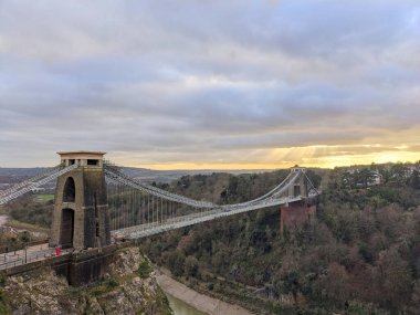 Bristol, İngiltere - 31 Ocak 2025: Tarihi Clifton Askı Köprüsü Avon Boğazı 'nı dramatik ve bulutlu bir gökyüzü altında uzanır ve güneş ışınları gün batımına yakın nehir vadisinin üzerinden geçer.