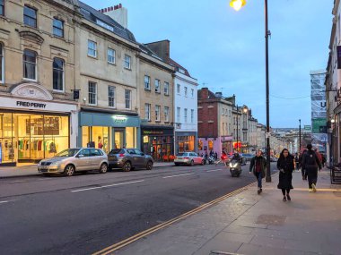 Bristol, İngiltere - 31 Ocak 2025: İnsanlar gün batımında bir şehir caddesi boyunca trafik ilerlerken dükkanların ve Gürcü binalarının önünden geçen kaldırımlarda yürüyor