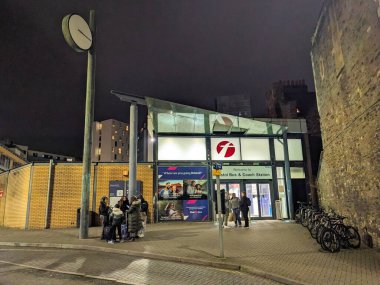 Bristol, İngiltere - 31 Ocak 2025: Geceleri Bristol Otobüs ve Koç İstasyonu 'nun dışındaki insanlar aydınlık girişi, park edilmiş bisikletleri ve karanlık gökyüzünün altında eski bir taş duvarı gösteriyorlar.