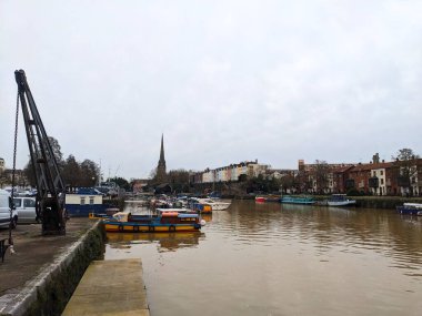 Bristol, İngiltere - 29 Ocak 2025: Limanda dar tekne ve feribotları, tarihi liman binalarını, yüksek bir kilise kulesini ve bulutlu bir günde büyük bir endüstriyel vinci gösteren görüntüler