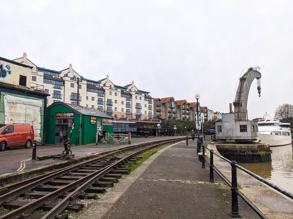 Bristol, İngiltere - 29 Ocak 2025: Bristol Limanı boyunca kullanılmayan tren rayları eğrisi, tarihi rıhtım yapılarını, modern rıhtım dairelerini ve bulutlu bir gökyüzü altında endüstriyel vinç geçişi