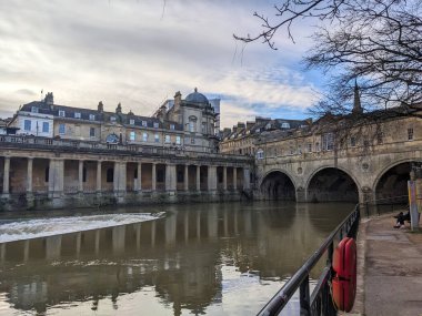 Bath, İngiltere - 30 Ocak 2025: Iconic Pulteney Köprüsü, tarihi Gürcü mimarisi Victoria Sanat Galerisi tarafından çerçevelenen Avon Nehri 'ni ve üzerinde çıplak dallar bulunan bulutlu bir kış gökyüzü altında bir Weir' ı kapsar.