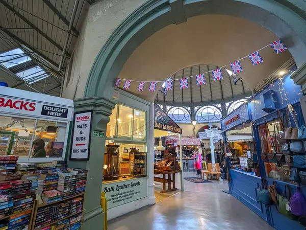 Bath, İngiltere - 30 Ocak 2025: Müşteriler, Bath Guildhall pazarındaki çeşitli tezgahlarda kitap, deri eşyalar ve çantalar satarak geleneksel perakende satış yerinde bayrak süsleyerek geziyorlar