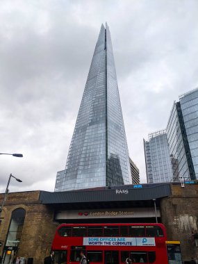 Londra, İngiltere - Temmuz 05 2022: Canlı kırmızı çift katlı bir otobüs, bulutlu bir gökyüzünün altında yükselen Çömlek ile Londra Köprüsü İstasyonu 'ndan geçiyor