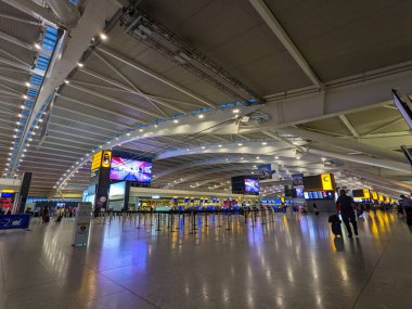 Londra, İngiltere - 03 Eylül 2022: Gezginler ve çalışanlar modern, ferah Heathrow Havaalanı Terminali 5 'ten geçerek kontrol gişelerinden ve bilgi içeren büyük ekranlardan geçiyorlar