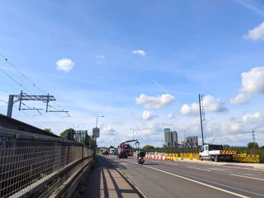 Londra, İngiltere - 19 Eylül 2021: Araçlar Forest Road boyunca inşaat bariyerleri ve kentsel arka planda modern binaların bulunduğu bir demiryolu ve kaldırımın yanında sürüyorlar