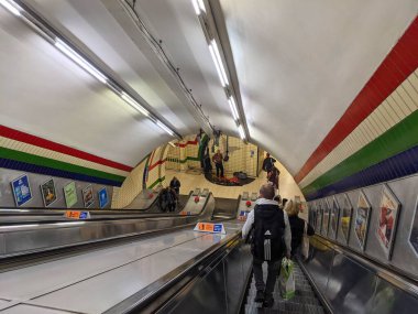 Londra, İngiltere - 30 Eylül 2021: Yolcular Piccadilly Circus istasyonuna uzun bir yürüyen merdivenden indiler, burada bir sokak müzisyeni en altta performans sergiliyor,