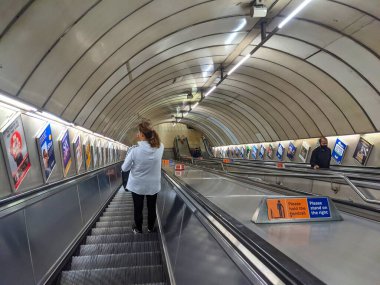 Londra, İngiltere - 23 Eylül 2021: Banliyö, Blackhorse Road Metro metro istasyonundan reklâm afişleriyle kaplı Viktorya Hattı platformuna doğru uzun bir yürüyen merdivenden iniyor