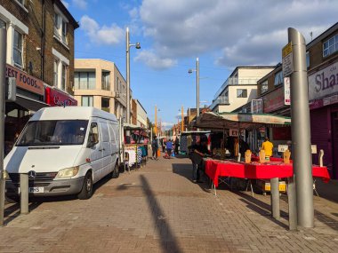 Londra, İngiltere - 19 Eylül 2021: Müşteriler ve satıcılar Londra 'da açık mavi bir gökyüzü altında mağazalarla dolu olan hareketli Walthamstow High Street' i çevreleyen renkli pazar tezgahlarında etkileşim halindeler