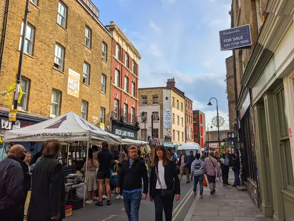Londra, İngiltere - 24 Eylül 2021: Müşteriler ve satıcılar pazar tezgahlarına bakıyorlar ve güneşli bir günde Brick Lane 'de çok katlı tuğla binalarla kaplı Brick Lane boyunca yürüyorlar