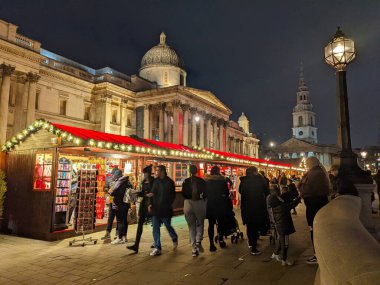 Londra, İngiltere - 21 Aralık 2021: İnsanlar, arka planda St. Martin Kulesi 'nin görülebildiği Ulusal Galeri' nin önündeki aydınlatılmış Noel market tezgahlarını araştırıyorlar.