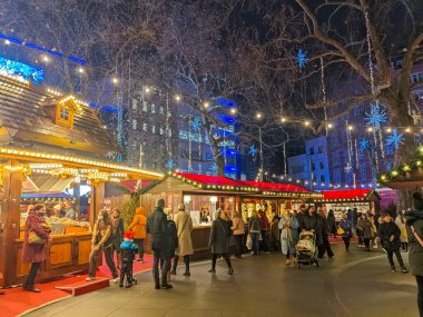 Londra, İngiltere - 21 Aralık 2021: İnsanlar Leicester Meydanı Noel pazarında parlak Noel ışıklarıyla aydınlatılmış şenlikli ahşap tezgahları toplayıp göz gezdiriyorlar ve canlı bir akşam ortamı yaratıyorlar.