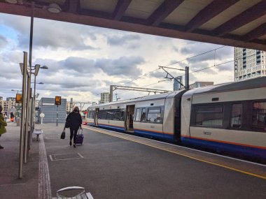 Londra, İngiltere - 24 Ekim 2021: Bavullu bir kişi Stratford istasyonunda bulutlu bir gökyüzünün altında metro platformu boyunca yürüyor