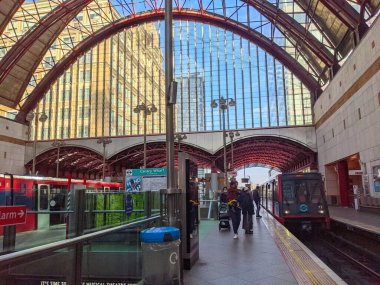 Londra, İngiltere - 24 Ekim 2021: Canary Wharf istasyonunda bekleyen işçiler, rıhtımdaki hafif tren istasyonlarına ulaşıp Kanarya Rıhtımı istasyonunun çarpan kemerli çatısı altında ayrılıyorlar.