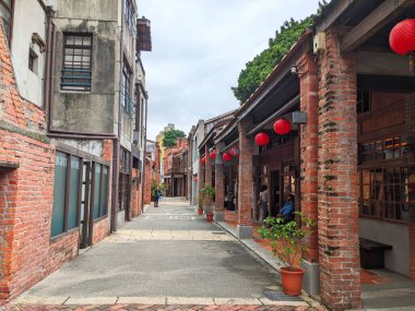 Taipei, Tayvan - 23 Kasım 2022: İnsanlar dükkanların önünden geçerken, Bopiliao Tarihi Bloğunda geleneksel kırmızı tuğla binalar ve dekoratif kırmızı fenerlerle kaplı dar bir sokak