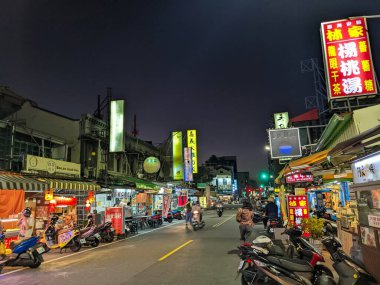 Tainan, Tayvan - 30 Kasım 2022: İnsanlar ve scooterlar, parlak ışıklı dükkanlar ve geceleri canlı bir atmosfer yaratan levhalarla dolu canlı bir caddeyi doldurdu