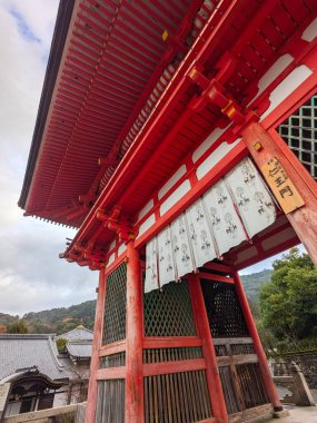 Kyoto, Japonya - 16 Aralık 2023: Canlı kırmızı ahşap Niomon ve bulutlu gökyüzü altındaki Kiyomizu-dera 'nın geleneksel mimari detaylarına yakından bakın