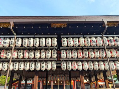 Kyoto, Japonya - 16 Aralık 2023: Japon yazıtları olan beyaz kağıt fenerler Yasaka Tapınağı 'ndaki geleneksel bir binanın karanlık saçaklarının altında gün ışığıyla aydınlatılıyor.