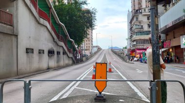 Hong Kong - 30 Temmuz 2021: Yan tarafında yaya köprüsü olan boş bir üstgeçit ve insanlar North Point 'teki işlek bir cadde ve tipik yüksek binalar boyunca bulutlu bir gökyüzü altında yürüyor
