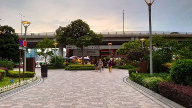 Hong Kong - 30 Temmuz 2021: Kuzey Noktası Feribot İskelesi yakınlarındaki bir şehir parkında yürüyen yayalar yemyeşil ve alacakaranlık üzerine bir köprü ile Kowloon City terminaline gidiyorlar.
