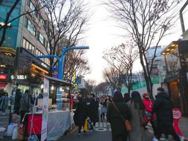 Seul, Güney Kore - 02 Şubat 2019: Yayalar Hongdae bölgesinde hareketli bir sokakta dükkanların ve bir sokak yiyecek satıcısının önünden geçtiler
