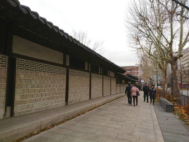 Seul, Güney Kore - Şubat 06 2019: İnsanlar başkentteki tarihi bir yapı kompleksinin bir parçası olan koyu kiremitli çatılı Unhyeongung 'un geleneksel taş duvarının yanında yürüyorlar