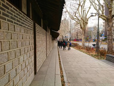 Seul, Güney Kore - Şubat 06: 2019: Yayalar bulutlu bir kış gününde işlek bir şehir sokağının yanında Unhyeongung 'un geleneksel taş duvarı boyunca yürürler