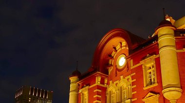 Tokyo, Japonya - 28 Ekim 2019: Tarihi Tokyo İstasyonu 'nun büyük kırmızı tuğla cephesi ve kubbeleri, Marunouchi ilçesinde ünlü bir mimari simge olan gece gökyüzünün altında sıcak bir şekilde parlıyor.