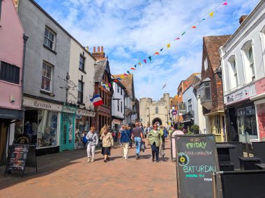 Canterbury, İngiltere - 19 Nisan 2025: İnsanlar coşkulu St. Peters Caddesi 'nde dükkanlar ve ortaçağ mimarisi ile Westgate' e doğru yürüyorlar.