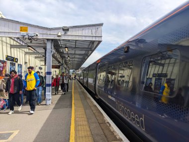 Canterbury, İngiltere - 19 Nisan 2025: Modern bir Güneydoğu yüksek hız treni kısmen bulutlu bir gökyüzü altında Canterbury West tren istasyonuna varırken, yolcuları ve gezginler platformda yürüyor