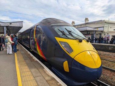 Canterbury, İngiltere - 19 Nisan 2025: Gökkuşağı üniformalı yüksek hızlı bir Javelin treni bulutlu bir gökyüzü altında yolcu beklerken Canterbury Batı İstasyonu platformunda duruyor