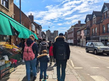 Canterbury, İngiltere - 19 Nisan 2025: Yayalar işlek St. Dunstans Caddesi boyunca ilerleyip tarihi Westgate Kuleleri 'ne doğru bulutlu açık mavi gökyüzü altında yürüyorlar.