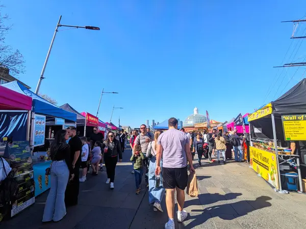 Londra, İngiltere - Nisan 05 2025: Birçok ziyaretçi, tarihi Greenwich Londra 'da açık mavi bir gökyüzü altında canlı Cutty Sark Street Food Market' te renkli gıda ve ürün tezgahlarına göz atıyor