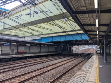 Osaka, Japonya - 09 Ağustos 2024: Boş bir şehir tren istasyonu platformu ve raylar, üstten kablolar ve demiryolu köprülerinden oluşan bir ağ altında uzanıyor