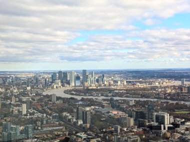 Londra, İngiltere - 16 Mart 2025: Yükseltilmiş bir perspektif Canary Wharf finans bölgesinin modern gökdelenlerini yakalıyor Thames Nehri 'nin kıvrımının yanındaki Londra ufuk çizgisine hakim olan