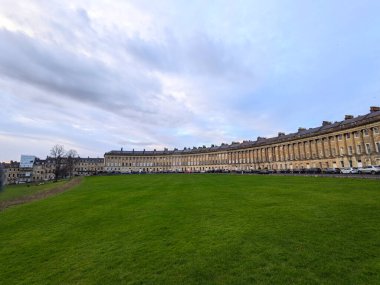 Bath, İngiltere - 30 Ocak 2025: Gürcistan mimarisinin bir başyapıtı olan ikonik Kraliyet Hilal 'i, tarihi şehirde karamsar bulutlu bir gökyüzünün altında engin yeşil çimlerin yanında zarif bir şekilde kıvrımlar.