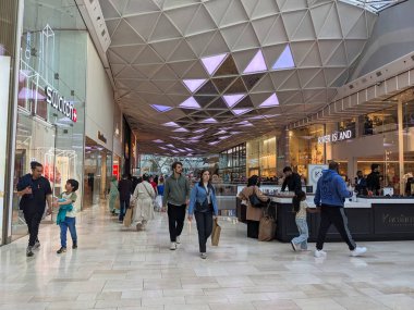 Londra, İngiltere - 26 Nisan 2025: Kalabalık Westfield Londra alışveriş merkezinin parlak ve modern iç kısımlarında, mağaza vitrinlerini ve yukarıda eşsiz mimari unsurları geçen çeşitli bir kalabalık hareket ediyor